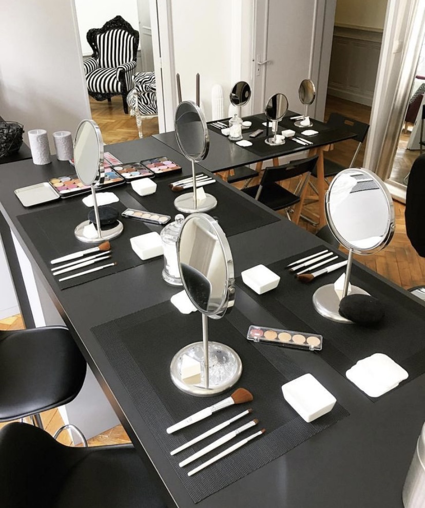 Mesa preparada con espejos, brochas y productos para una clase de maquillaje.